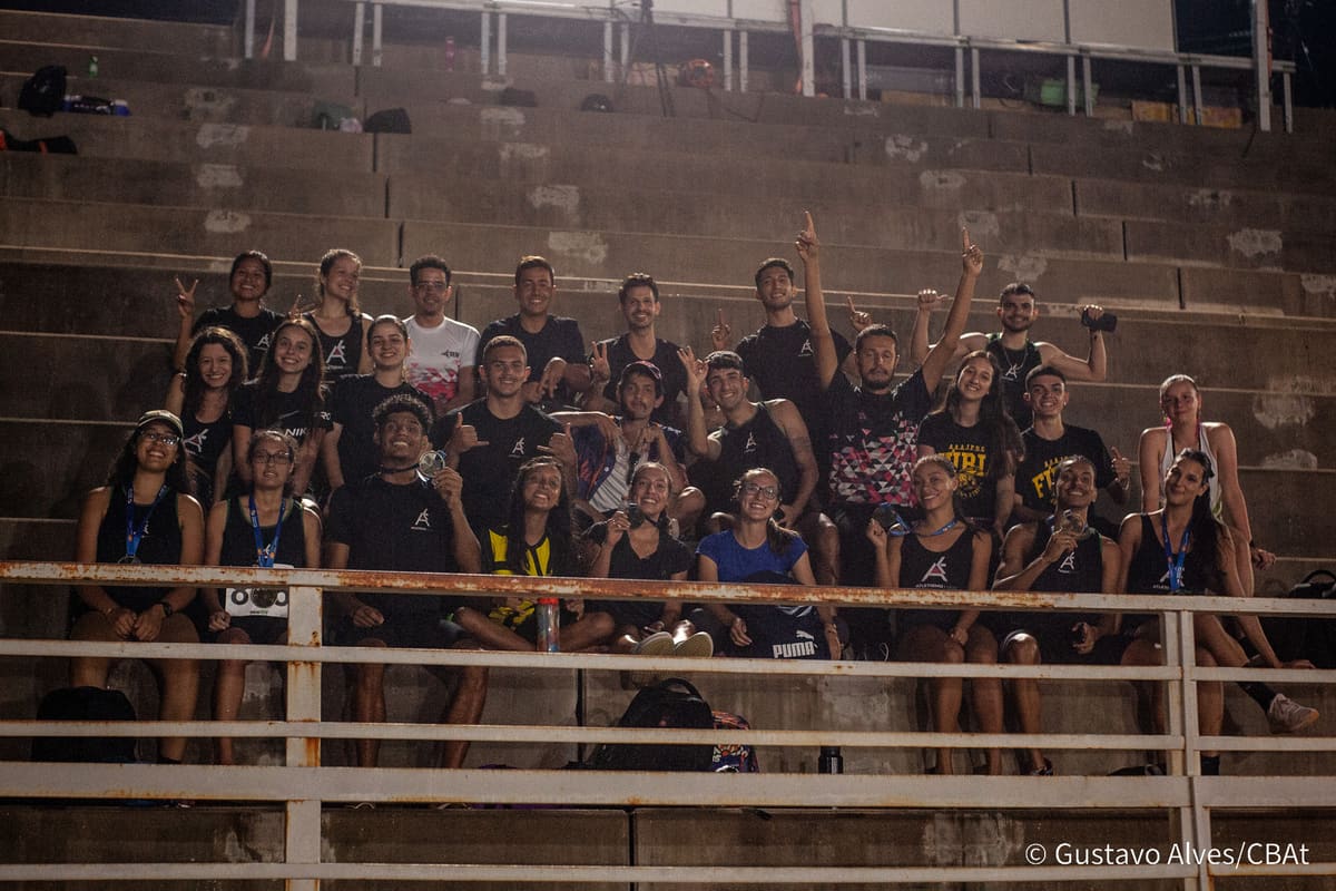 Equipe da Atletismo-UEM reunida na arquibancada à noite, foto em grupo