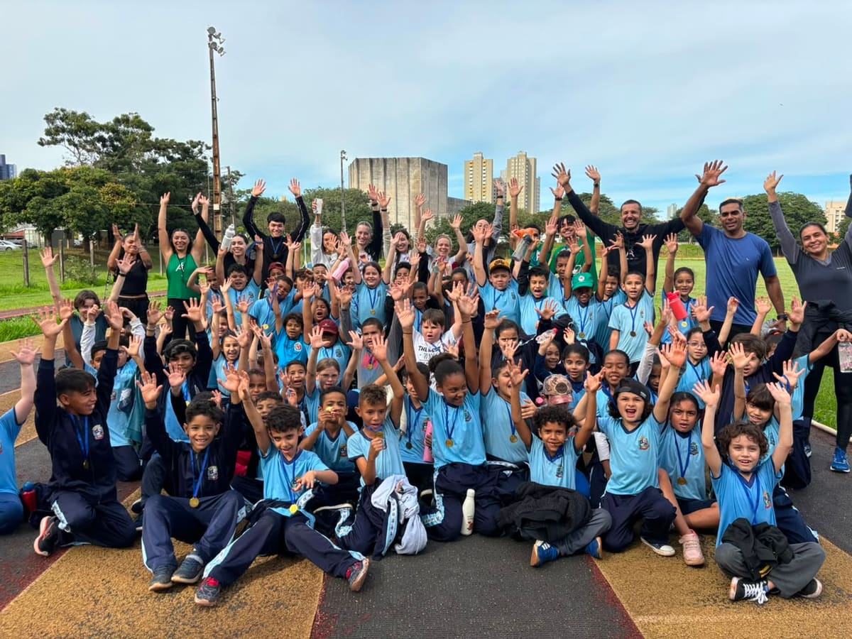 Alunos de escola pública comemorando com medalhas na Pista de Atletismo da UEM, ao lado de integrantes do projeto Atletismo UEM